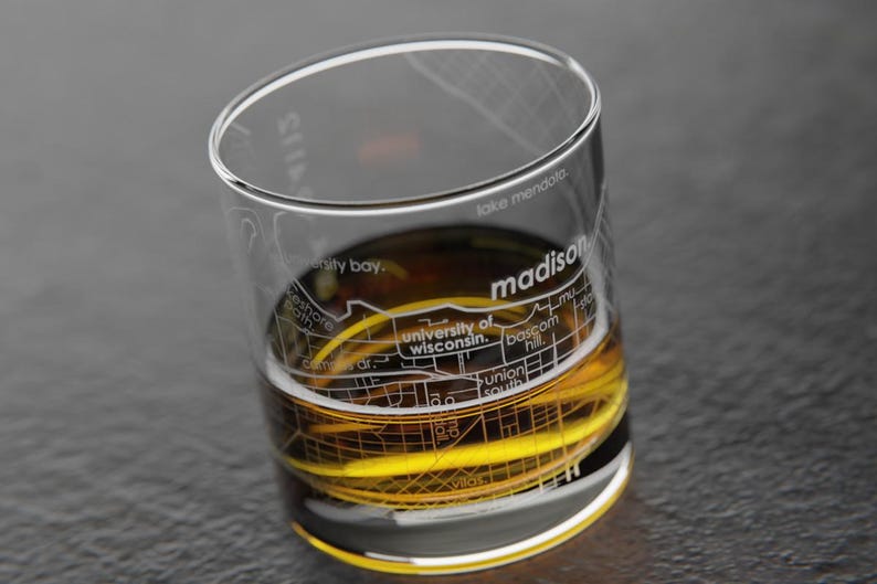 May include: A clear glass with a map of Madison, Wisconsin etched on the side. The glass is filled with a golden liquid.