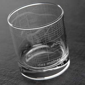 May include: A clear glass tumbler with an etched design of the city of Des Moines, Iowa. The design includes street outlines and the words "Capitol East" and "Des Moines".