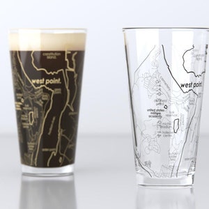 May include: Two clear glass pint glasses with a black and gold map of West Point, New York printed on them. The map includes the text "West Point" and "United States Military Academy".
