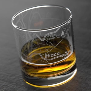 May include: A clear glass rocks glass with a detailed etched map of Ithaca, New York. The glass is filled with amber-colored liquid.