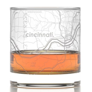 May include: A clear glass with a map of Cincinnati, Ohio etched on the side. The glass is filled with amber liquid. The map includes the neighborhoods of Westwood, Clifton, Covington, and Bellvue.
