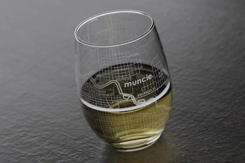 May include: A clear glass wine glass with a design of the Muncie, Indiana city map etched into the side. The glass is filled with a light-colored beverage.