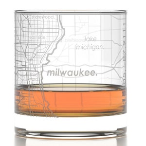 May include: A clear glass with a map of Milwaukee, Wisconsin etched on the side. The glass is filled with amber liquid. The text "milwaukee." is visible at the bottom of the glass.