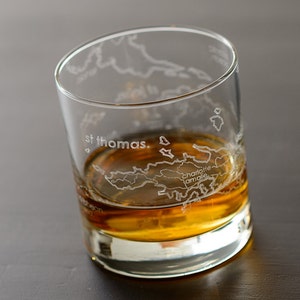 May include: A clear glass with an etched map of the Virgin Islands, including St. Thomas and Charlotte Amalie, filled with amber-colored liquid.