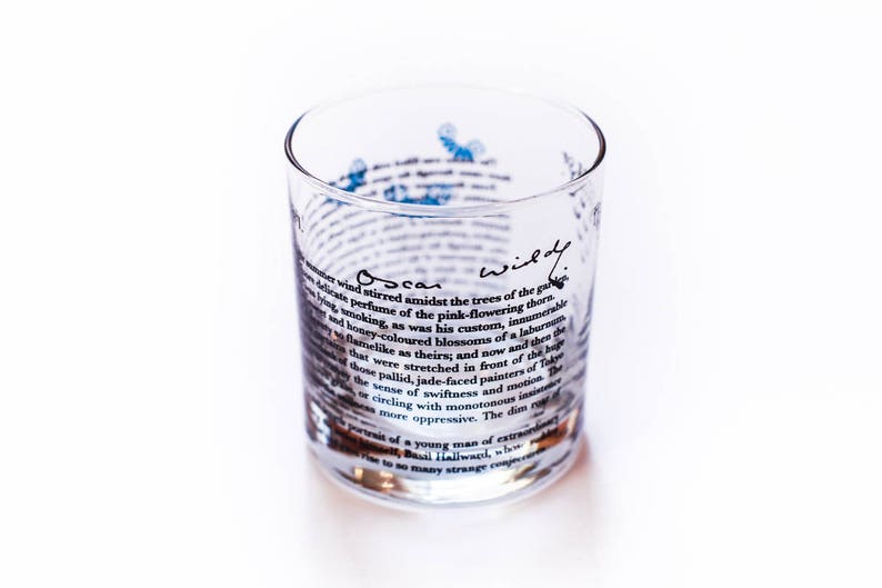 May include: A clear glass tumbler with a quote from Oscar Wilde printed on the side. The quote reads: "A delicate wind stirred amidst the trees of the garden, and honey-coloured blossoms of a laburnum that were stretched in front of the huge sense of swiftness and motion. The dim insistent"