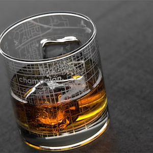 May include: A clear glass with an etched map of Champaign, Illinois, filled with amber liquid and ice cubes.