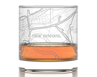 May include: A clear glass with an etched map of New Orleans and the text "new orleans." The glass is filled with a brown liquid.