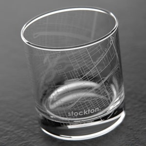 May include: A clear glass with an etched design of the Stockton, California city map. The glass has a rounded bottom and the words "stockton." are etched on the bottom.