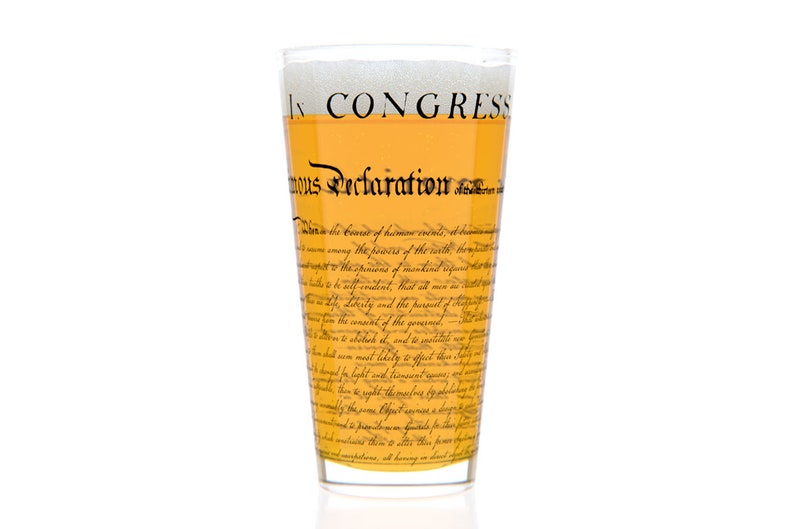 May include: A tall glass filled with a light yellow liquid, with a white head of foam. The glass is printed with the text "In Congress, July 4, 1776.  Unanimous Declaration of the thirteen united States of America."