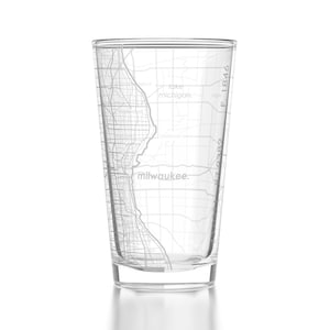 May include: A clear glass with a map of Milwaukee, Wisconsin printed on the side. The map includes the city's streets, lakes, and surrounding areas. The text "milwaukee." is printed at the bottom of the map. The glass is empty and has a reflective surface.
