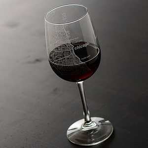 May include: A clear wine glass with a map of Chicago etched into the side. The glass is filled with red wine. The text "chicago" is printed on the side of the glass.