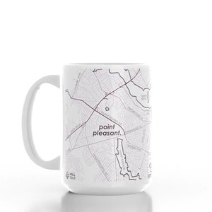 K&ouml;nnte beinhalten: Wei&szlig;e Keramiktasse mit einer Schwarzwei&szlig;karte von Point Pleasant, West Virginia. Der Text "point pleasant." ist in Lila auf die Tasse gedruckt.