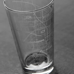 May include: A clear glass with an etched map of Tallahassee, Florida. The map includes street names and the city's name.