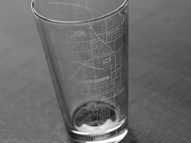 May include: A clear glass with an etched map of Tallahassee, Florida. The map includes street names and the city's name.