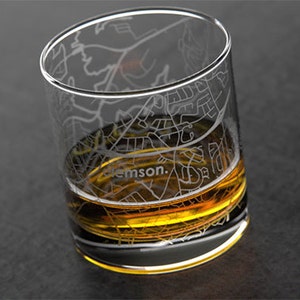 May include: A clear glass with an etched design of the city of Clemson, South Carolina. The glass is filled with a golden amber liquid.