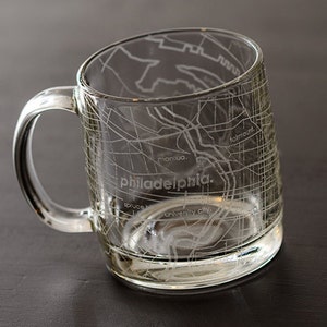 May include: A clear glass mug with a handle, featuring an etched design of the Philadelphia city map. The map includes street names like "Manayunk" and "University City".