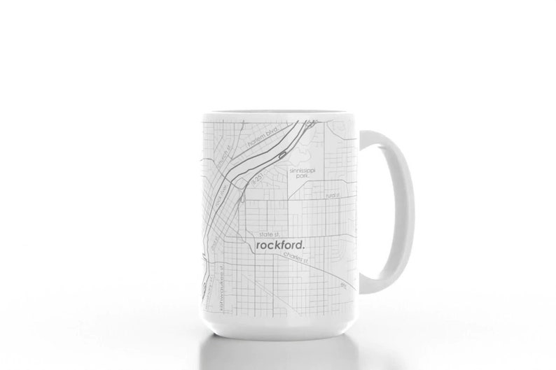 K&ouml;nnte beinhalten: Eine wei&szlig;e Keramiktasse mit einer schwarz-wei&szlig;en Karte von Rockford, Illinois, die darauf gedruckt ist. Die Karte zeigt die Stra&szlig;en der Stadt und den Rock River. Der Text "rockford." ist in Schwarz unter der Karte gedruckt.