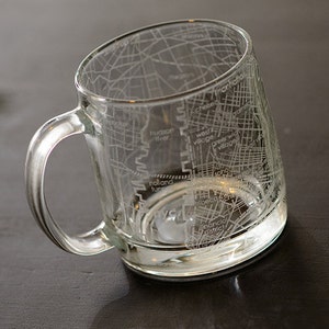 May include: A clear glass mug with a map of New York City etched on the side. The map includes the names of neighborhoods like "Greenwich Village", "Financial District", and "West Village".