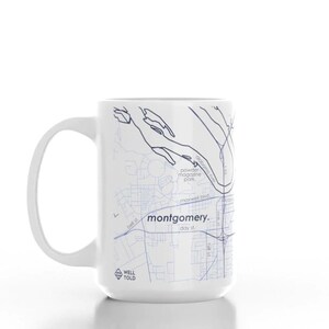 K&ouml;nnte beinhalten: Wei&szlig;e Keramiktasse mit einer blauen und wei&szlig;en Karte von Montgomery, Alabama. Die Tasse tr&auml;gt den Text "montgomery." und "WELL TOLD".