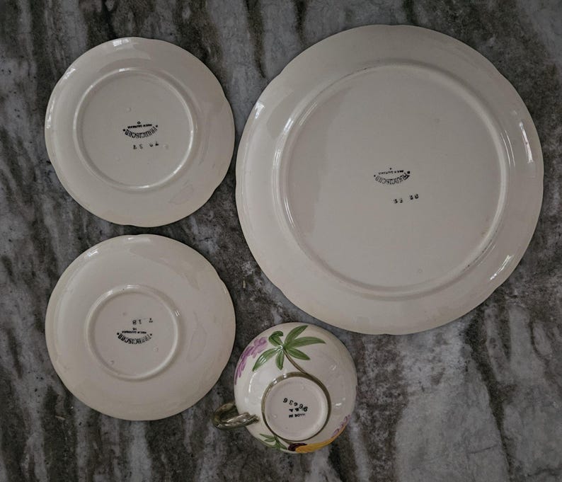 Puede incluir: Juego de cuatro platos vintage de cer&aacute;mica blanca con dise&ntilde;os florales. Los platos tienen un borde elevado y un borde festoneado. Los platos est&aacute;n marcados con las palabras "Made in Japan" y "Hand Painted".