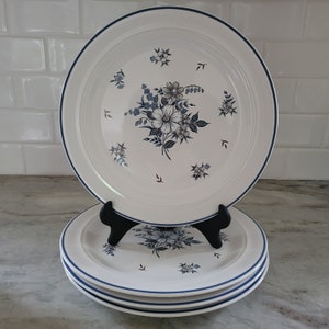 Puede incluir: Tres platos de cena de cerámica blanca con un diseño floral azul y blanco. Los platos están apilados uno encima del otro.