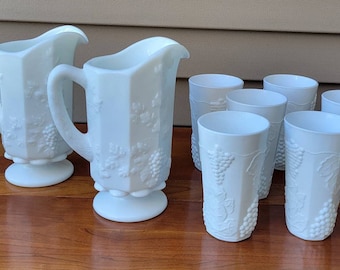 May include: Set of eight white milk glass pieces with a grapevine design. The set includes two pitchers and six glasses.