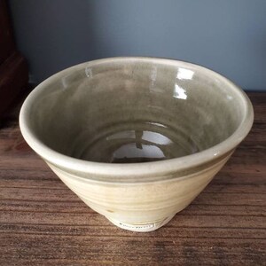 May include: A light green ceramic bowl with a white rim and a light brown base. The bowl is glazed and has a slight sheen.