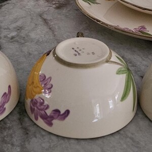 Puede incluir: Tres tazas de t&eacute; de cer&aacute;mica blanca con dise&ntilde;os florales. Las tazas presentan flores amarillas, moradas y verdes sobre un fondo blanco. Las tazas son todas ligeramente diferentes, pero tienen el mismo dise&ntilde;o general.
