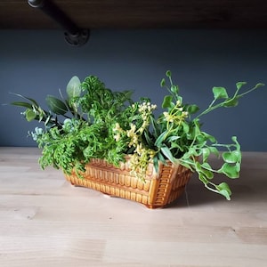 Könnte beinhalten: Ein brauner Keramiktopf mit strukturiertem Design, gefüllt mit verschiedenen grünen Pflanzen und gelben Blumen.