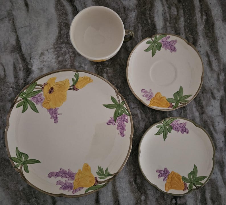 Puede incluir: Un juego de porcelana floral vintage con un dise&ntilde;o de flor amarilla y lupino morado. El juego incluye una taza de t&eacute;, un platillo y dos platos.