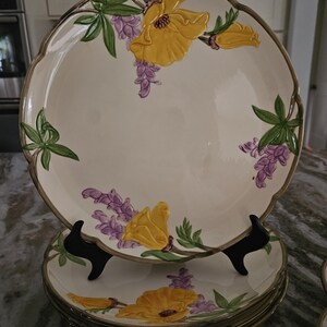 Puede incluir: Un juego de platos de cena vintage con flores con un dise&ntilde;o floral amarillo y morado. Los platos est&aacute;n apilados uno encima del otro y tienen un borde festoneado.
