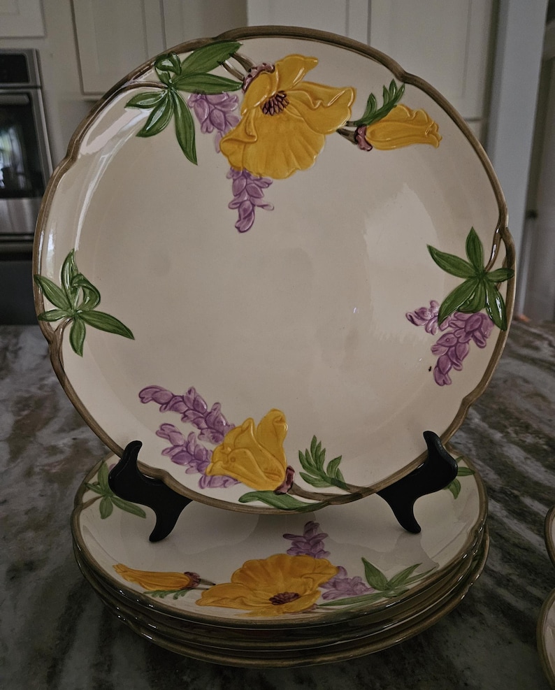 Puede incluir: Un juego de platos de cena vintage con flores con un dise&ntilde;o floral amarillo y morado. Los platos est&aacute;n apilados uno encima del otro y tienen un borde festoneado.