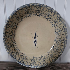 Puede incluir: Un plato para tarta grande, redondo y de cerámica con un esmalte moteado azul y blanco. El plato tiene un sencillo diseño de trigo azul en el centro.