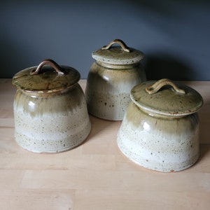 May include: Three ceramic canisters with lids in shades of brown and white. The canisters have a speckled glaze and are perfect for storing kitchen staples.