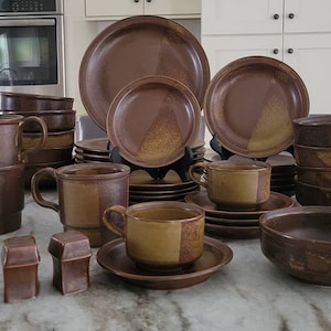 May include: A set of brown and tan stoneware dinnerware with a checkered pattern. The set includes plates, bowls, mugs, and saucers.