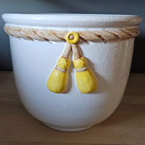 May include: White ceramic planter with a rope design around the top and two yellow tassel-like decorations.