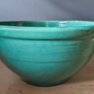 Peut inclure: Un bol mélangeur en céramique vert turquoise avec une surface lisse et arrondie. Le bol est vide et a un léger éclat.