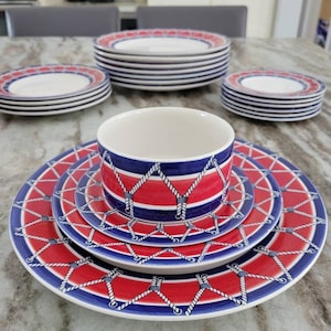 May include: A nautical-themed dinnerware set featuring red and blue patterns. The set includes plates and a bowl, all with a rope and knot design. The plates have a white border with a blue stripe. The bowl has a similar design.