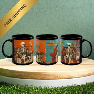 May include: Three black coffee mugs with a skeleton design. Each mug features a skeleton sitting in a chair with a cigar and a cup of coffee. The mugs have a black background with a colorful design.