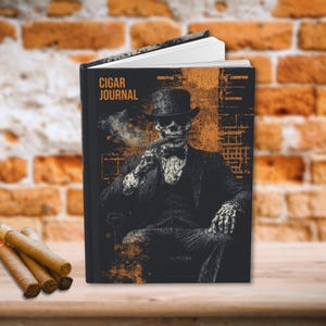 May include: A black journal with a skull wearing a top hat and sunglasses smoking a cigar. The journal cover has the text "CIGAR JOURNAL" in white letters.