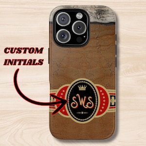 May include: A brown and gold iPhone case with a cigar band design. The band has a red and white star pattern and a gold crown with the initials "SWS" in the center.