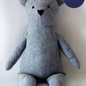 May include: A handmade, light blue teddy bear plush toy. The bear has a stitched face with dark blue eyes and nose. The bear is made of a textured fabric and has the words "INSTANT DOWNLOAD PDF" in a blue circle.