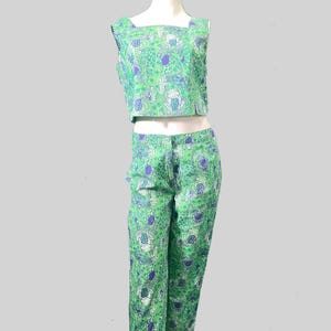 May include: A two-piece outfit featuring a crop top and capri pants. The set is adorned with a green and purple floral pattern. The top has a square neckline, and the pants have a straight leg cut. The outfit is displayed on a mannequin.