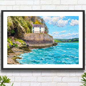May include: A framed landscape painting featuring a white house perched atop a stone seawall overlooking turquoise water. The scene includes a rocky shoreline with green foliage, a bright blue sky with textured white clouds, and distant green hills.