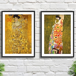 May include: Two framed art prints featuring Gustav Klimt paintings. One print showcases a woman in a gold dress with geometric patterns. The other depicts a woman in a colorful dress with circular and organic shapes, set against a green background.