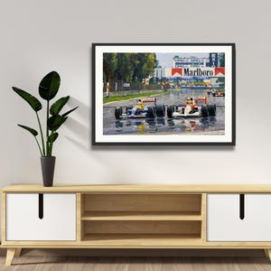 Puede incluir: Obra de arte enmarcada que representa una carrera de F&oacute;rmula 1 bajo la lluvia. La pintura muestra varios coches de carreras en una pista mojada, con el logotipo de Marlboro en el fondo. La obra de arte se exhibe sobre un mueble de madera.