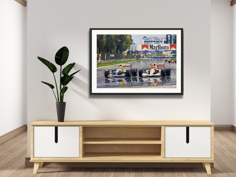 Puede incluir: Obra de arte enmarcada que representa una carrera de F&oacute;rmula 1 bajo la lluvia. La pintura muestra varios coches de carreras en una pista mojada, con el logotipo de Marlboro en el fondo. La obra de arte se exhibe sobre un mueble de madera.