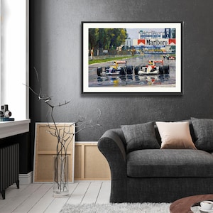 Puede incluir: Obra de arte enmarcada que representa una carrera de F&oacute;rmula 1. La pintura muestra varios coches de carreras en una pista mojada, con el logotipo de Marlboro en el fondo. La obra est&aacute; enmarcada en negro y cuelga de una pared gris oscura.