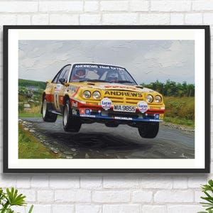 Op de afbeelding: Een ingelijste print van een vintage rallywagen in de lucht. De auto is geel, rood en blauw met de tekst "ANDREWS Heat for Hire" en het kenteken "WIA 9855". De afbeelding is tegen een landschap geplaatst.