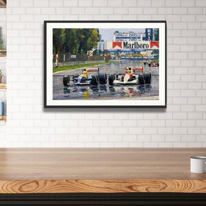 Puede incluir: Obra de arte enmarcada que representa una carrera de F&oacute;rmula 1. Dos coches de carreras est&aacute;n en primer plano, con el logotipo de Marlboro visible en el fondo. La pista est&aacute; mojada, reflejando los coches y el entorno.